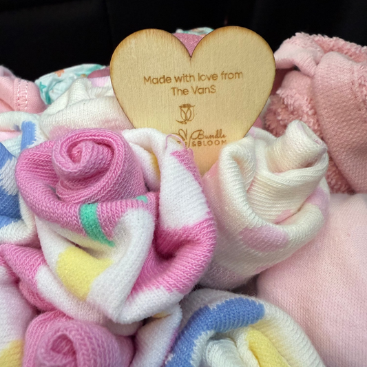 Stack of colorful baby socks with a wooden heart tag on a dark background